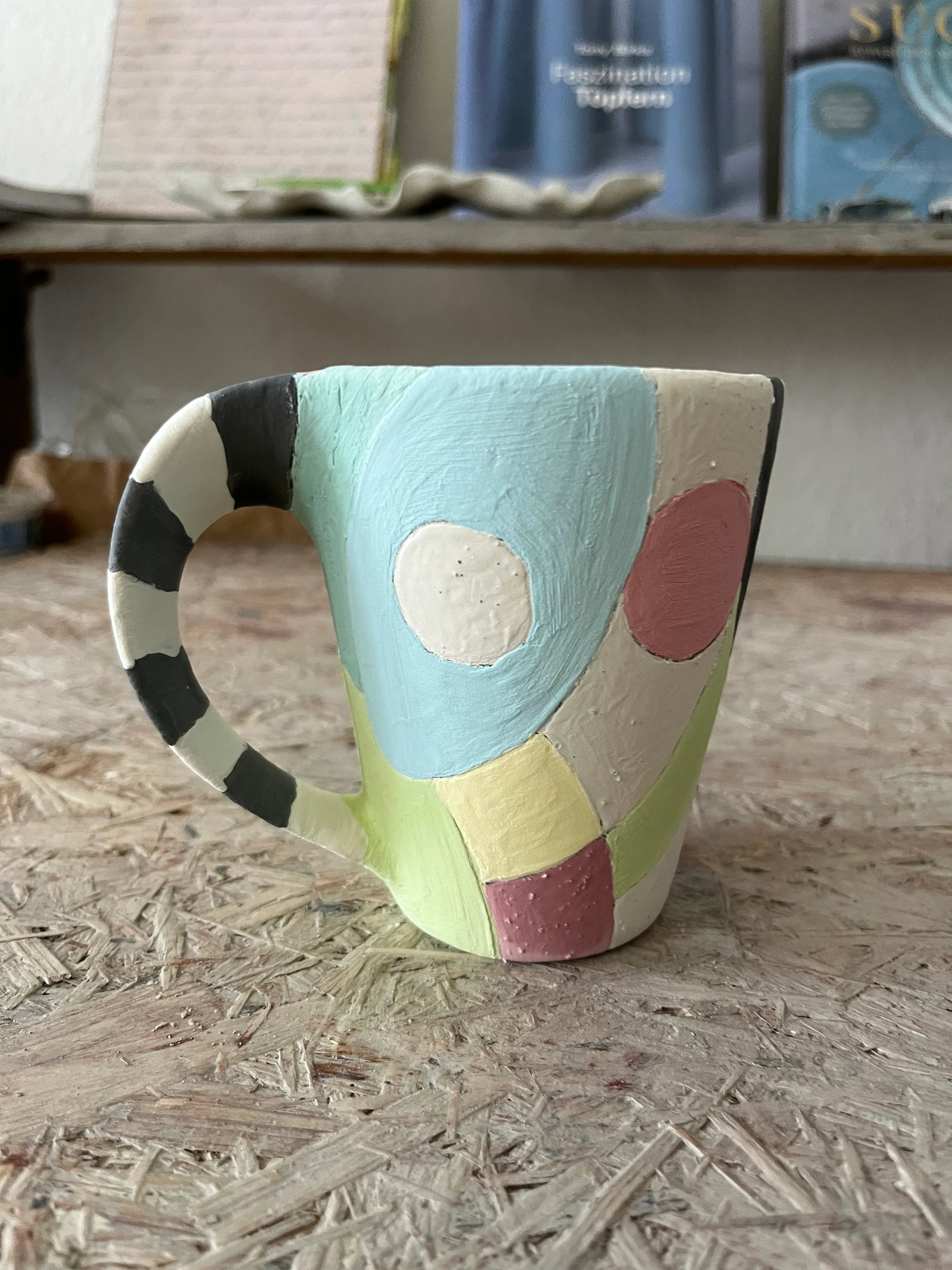 Bunter Becher auf Holztisch mit Büchern dahinter.