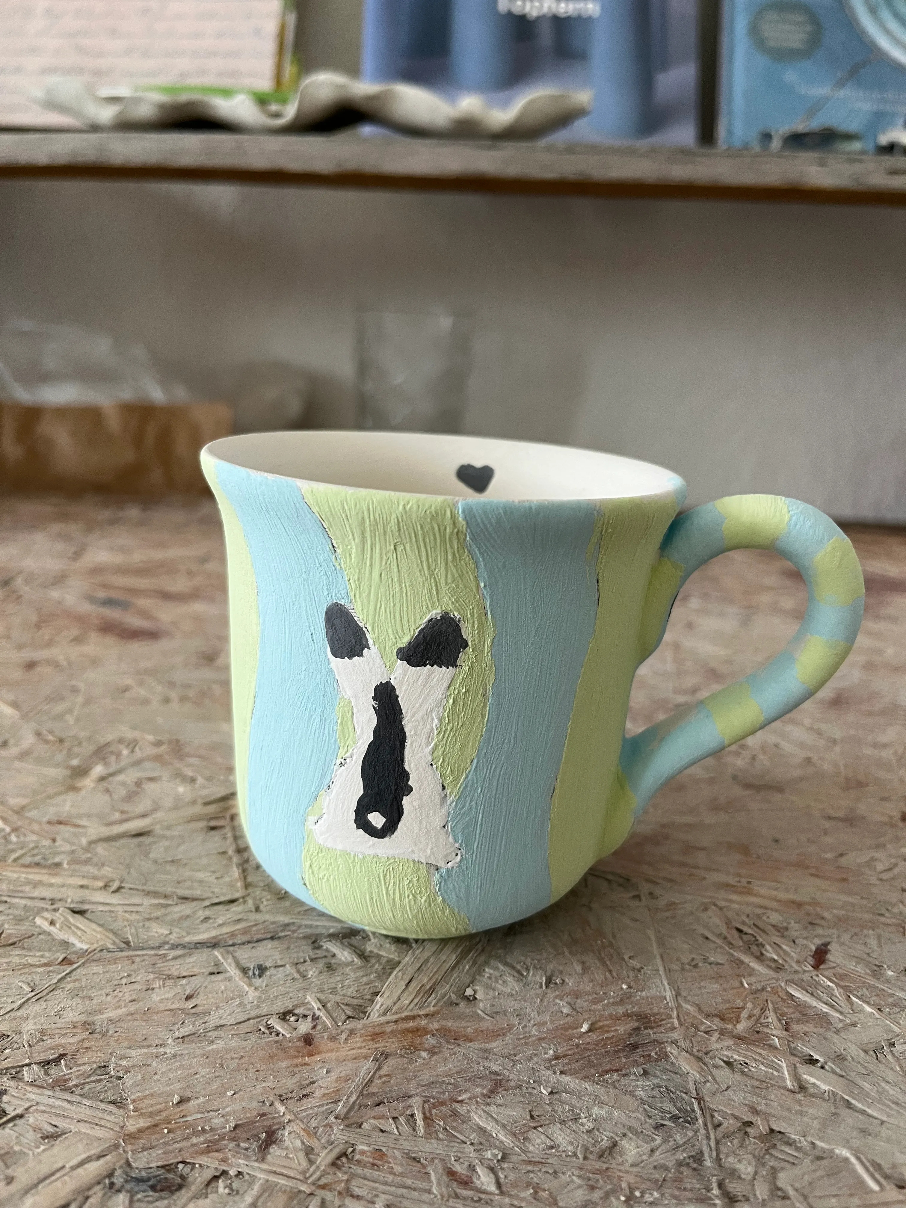 Bunter Becher mit Kuhbild auf Tisch.