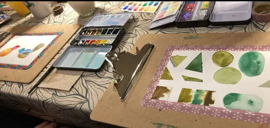 Watercolor shapes painted on clipboards at table.