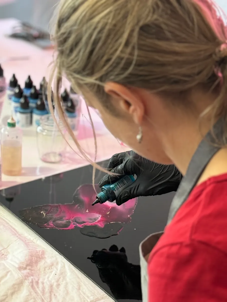 Woman applying pink paint on black canvas.