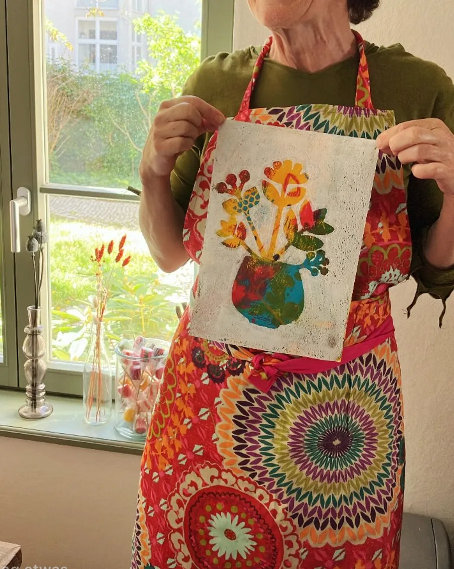 Person hält Blumenbild drinnen am Fenster.