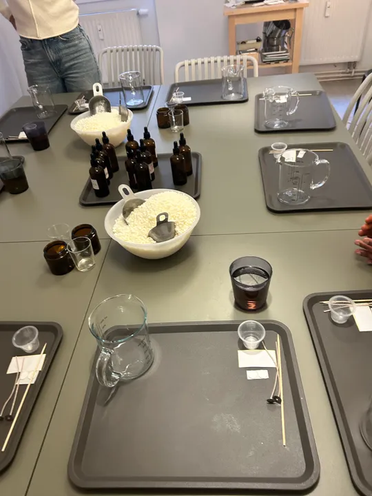 Tisch mit Kerzenherstellungszubehör, Gläsern und Tabletts.