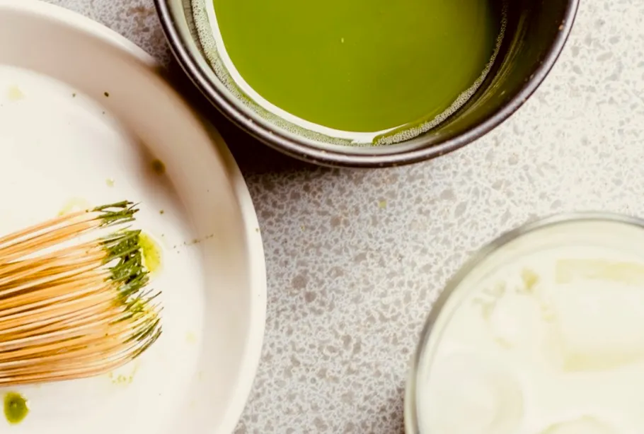 Matcha-Besen neben Schalen mit Matcha und Milch.