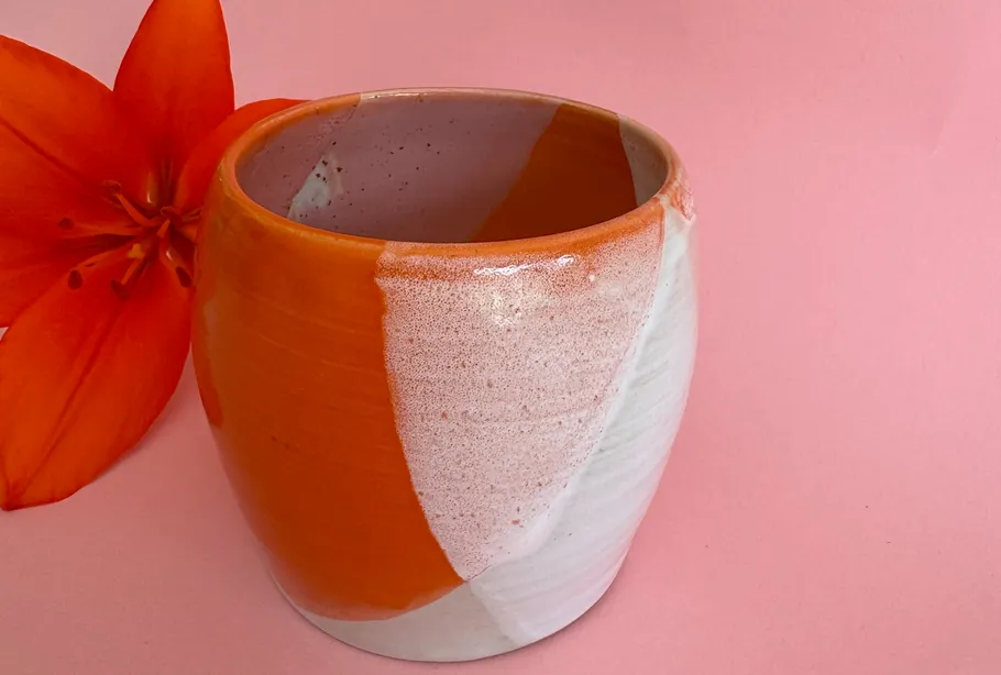 Oranger Tongefäß mit Blume auf rosa Hintergrund.