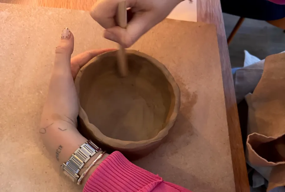 Hände formen Tontopf auf Holztisch.