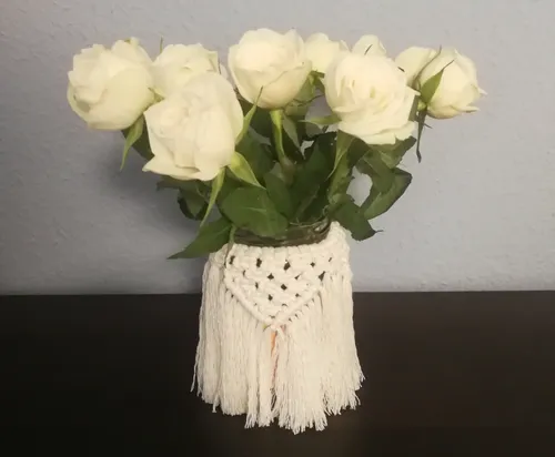 White roses in macrame-decorated jar on table.