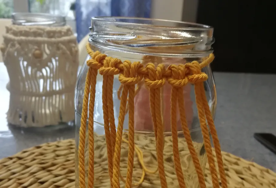 Glasgefäß mit gelben Macrame-Bändern befestigt.