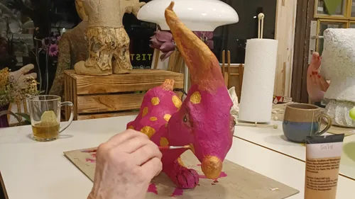 Person painting pink sculpture with gold dots.