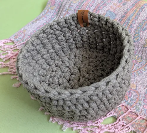 Gray crocheted basket on patterned fabric.