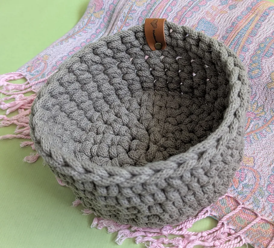 Gray crocheted basket on patterned fabric.
