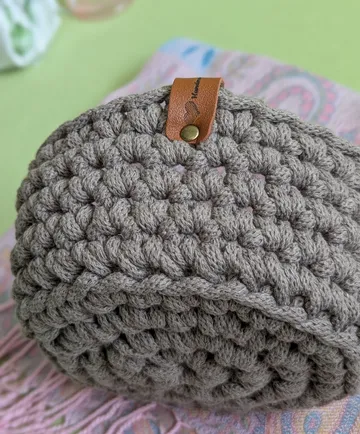Gehäkelte braune Tasche mit Lederetikett, verschwommener Hintergrund.