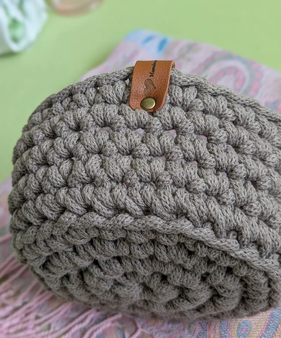 Crocheted brown bag with leather label, blurred background.