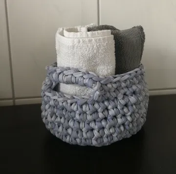 Gehäkelter Korb mit Handtüchern auf einem Regal.