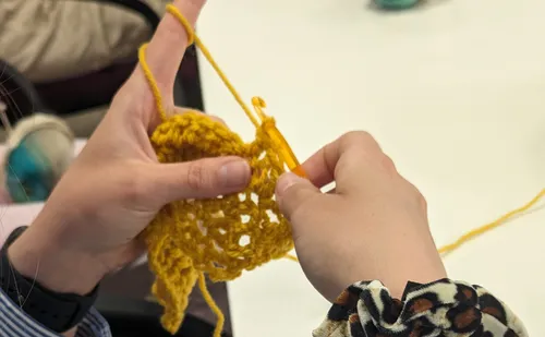 Hands crocheting yellow yarn at a table.