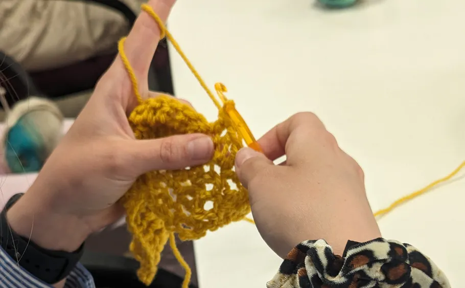 Hands crocheting yellow yarn at a table.