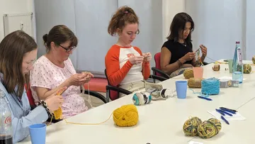 Four women knitting around a conference table.