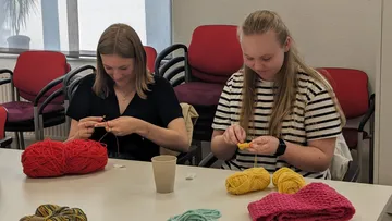 Zwei Personen stricken mit buntem Garn drinnen.