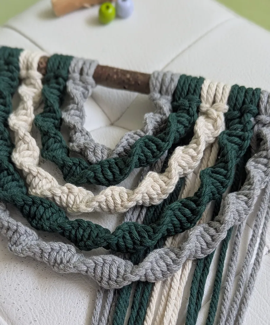 Macrame knots in green, white, gray on branch.