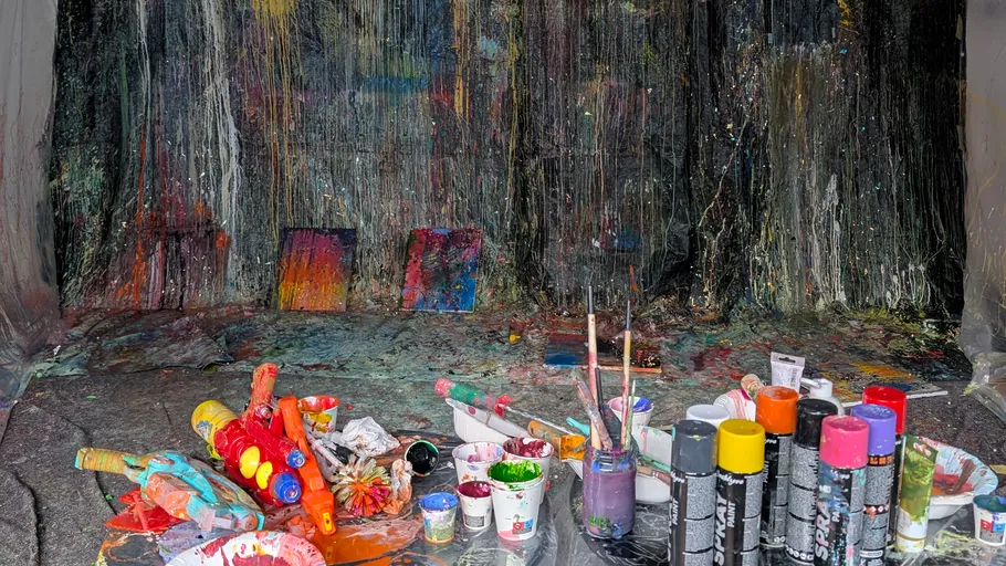 Unordentliches Malstudio mit verstreuten Farbvorräten.