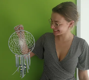 Woman smiles holding dreamcatcher against green wall.