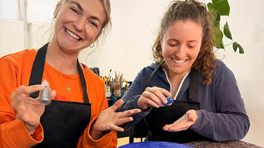 Two women applying paint on hands in studio.