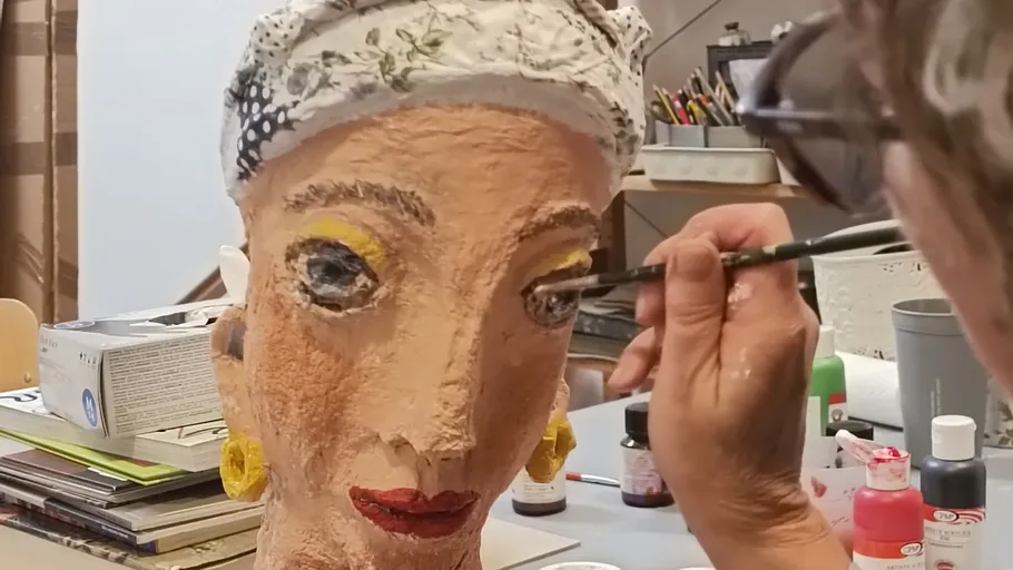 Person painting a sculpted head indoors.