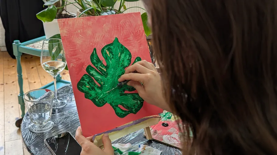 Person malt grünes Blatt auf rosa Leinwand.