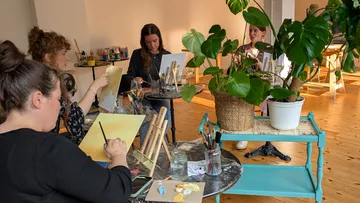 People painting in a room with plants.