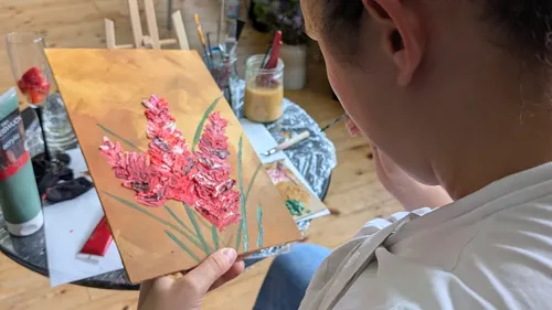 Person painting flower with acrylic on easel.