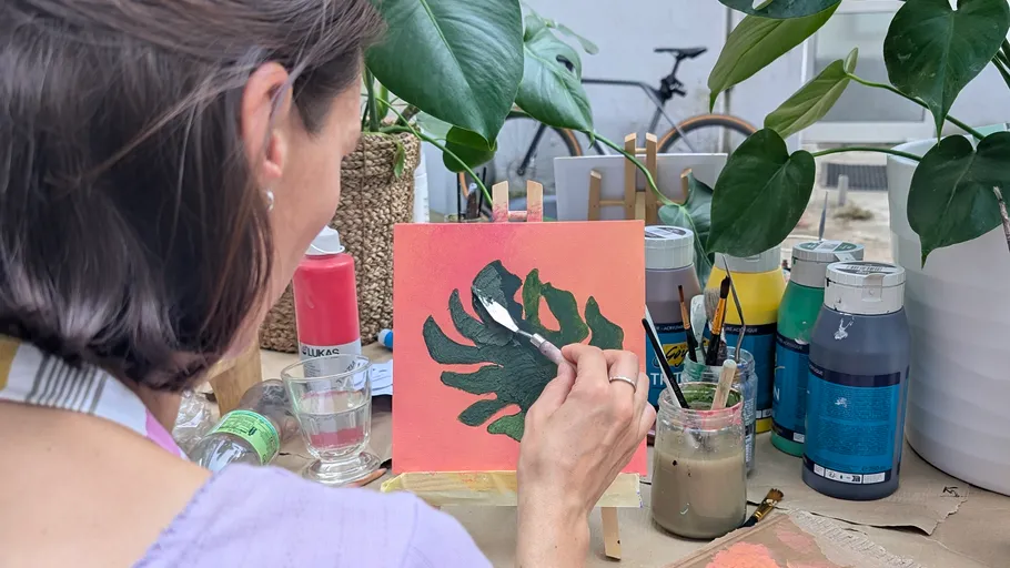 Person painting plant on small canvas outdoors.