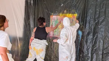 Two people painting on a canvas in studio.