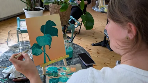 Person painting plant on canvas indoors.