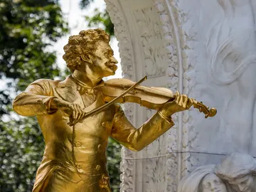 Goldene Statue spielt Geige vor einer kunstvollen Kulisse.