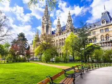 Historisches Gebäude steht neben grünem Park mit Bänken.