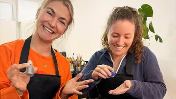 Two women smiling while crafting indoors.