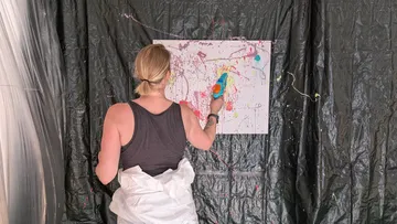 Person spray-painting canvas in messy studio.