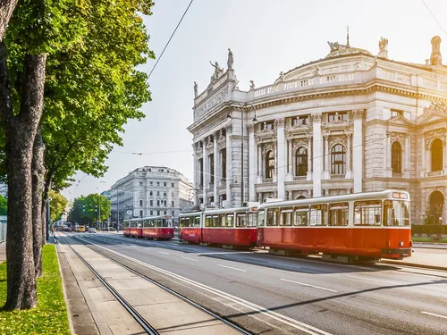 Rote Straßenbahnen fahren vor einem historischen Gebäude.