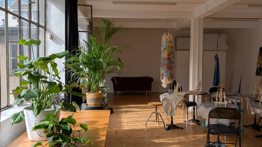 Sunlit art studio with plants and furniture.