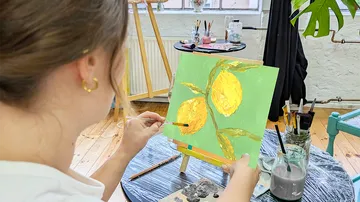 Person painting lemons on canvas indoors.