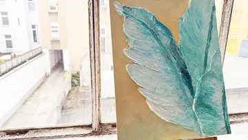 Textured artwork on easel by window.