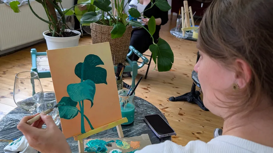 Person painting leaves on a canvas indoors.
