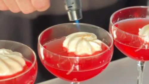 Hand torching cream on red cocktails.