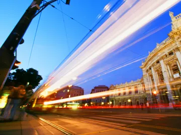 Straßenbahn fährt schnell vor historischer Gebäude-Fassade bei Nacht.