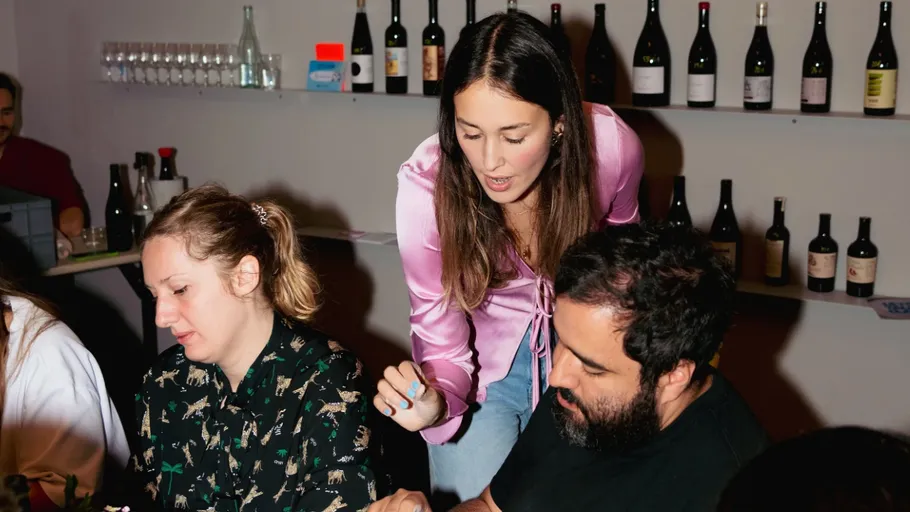 Three people conversing at a table with wine bottles.