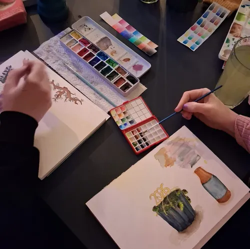 Hands painting with watercolors on paper.