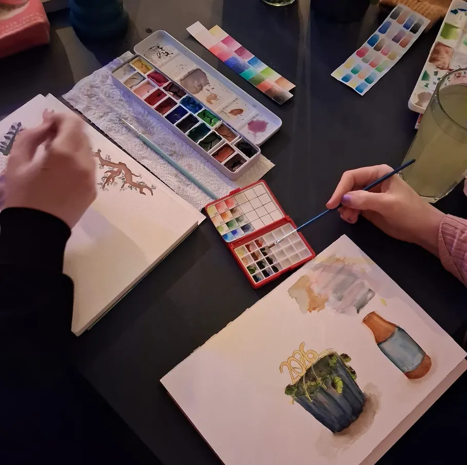 Hände malen mit Aquarellfarben auf Papier.