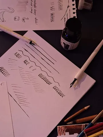 Kalligrafieübung mit Stiften und Tinte auf Papier.