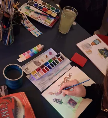 Person malt mit Aquarellfarben auf Tisch.