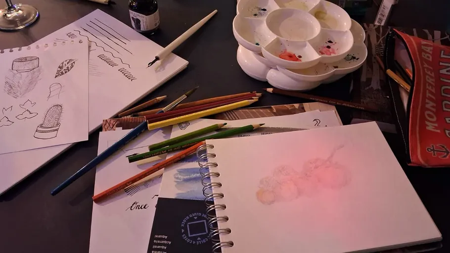 Skizzenbuch mit Buntstiften und Farbe auf Tisch.