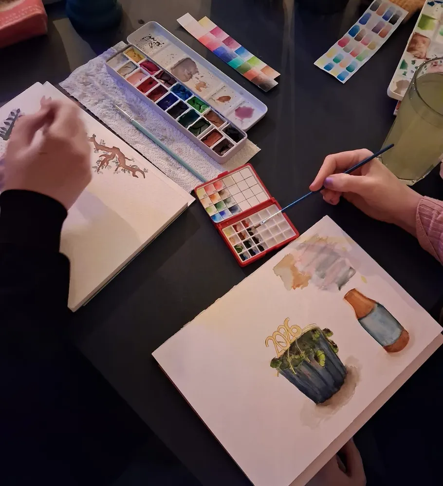 Personen malen mit Aquarellfarben an einem Tisch.